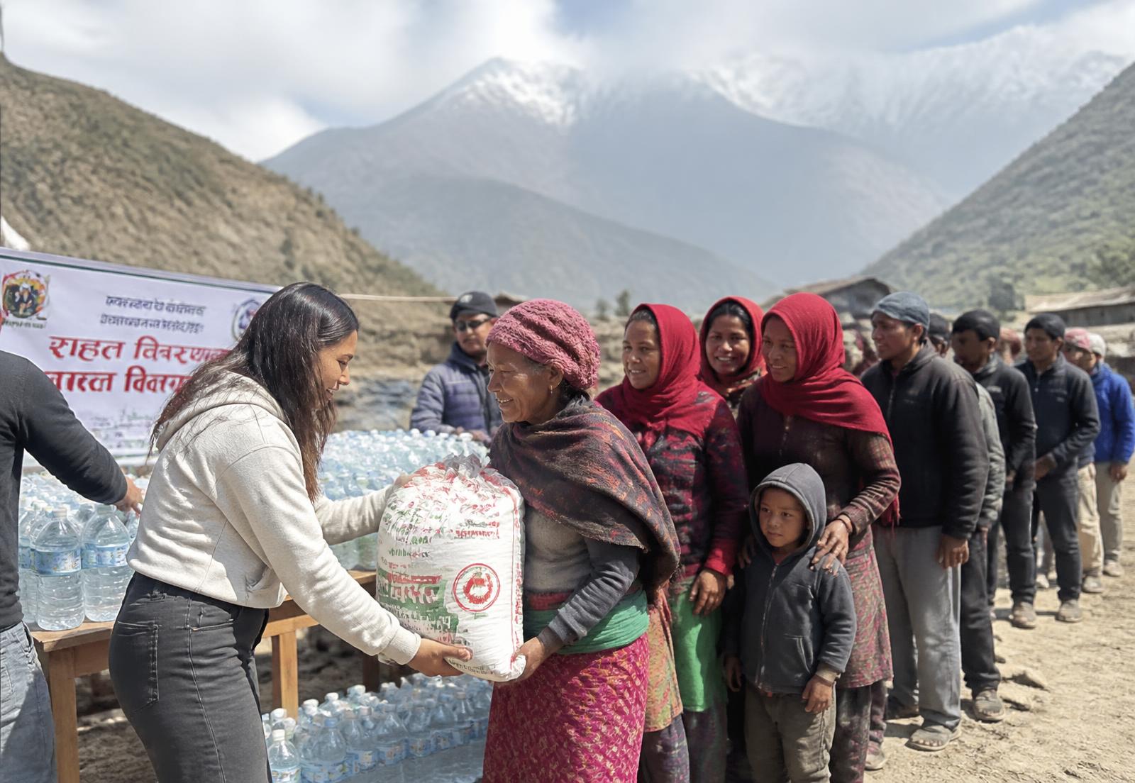 Volunteers handing rice and bottled water to villagers at a relief distribution point in Nepal